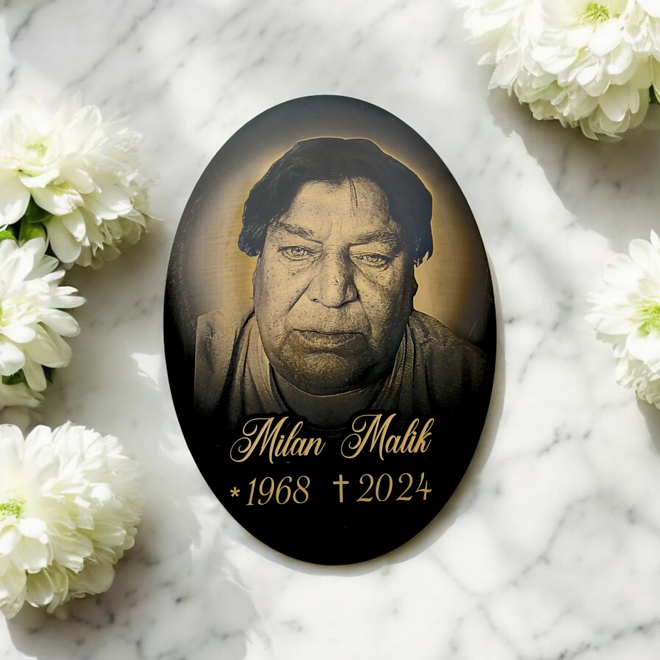 schwarzes ovales Grabschild mit Foto auf Marmor mit Blumen
